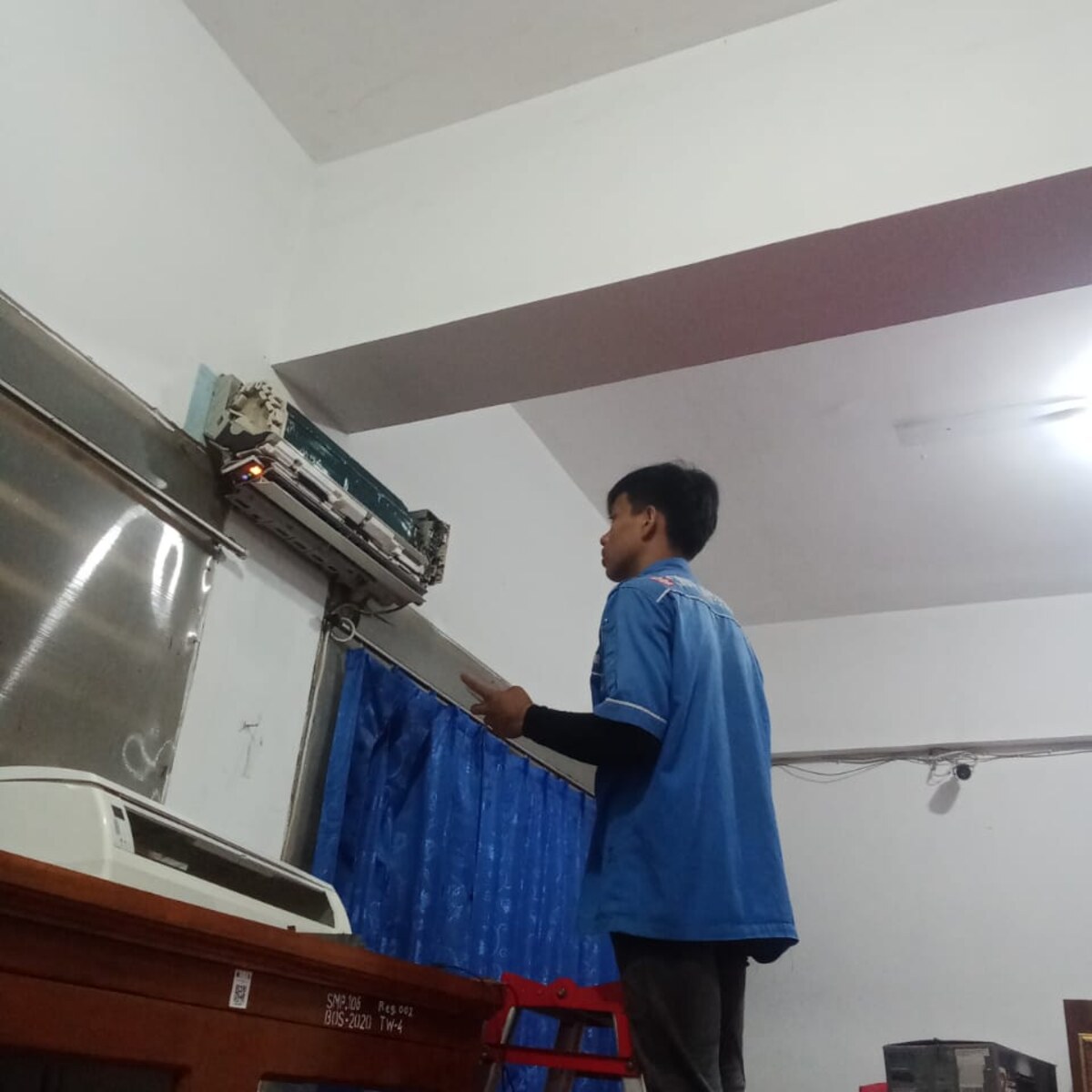 Teknisi Mandiri Utama Electro berseragam biru sedang memperbaiki AC di rumah pelanggan